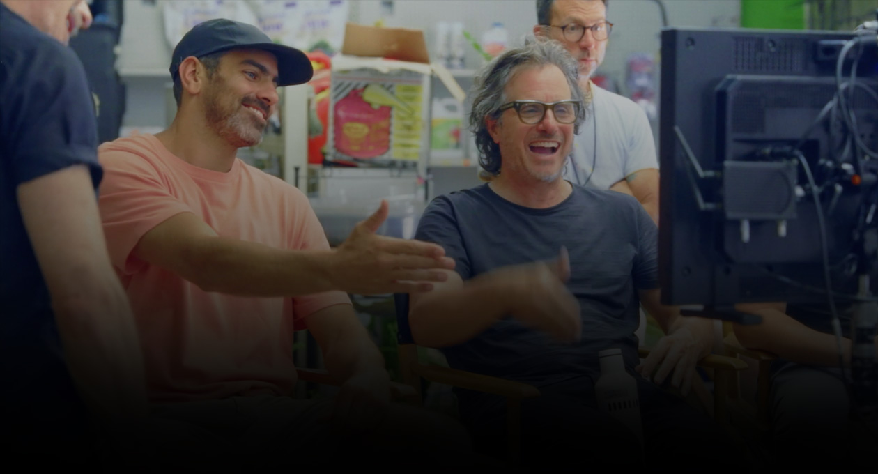 Image of two seated male filmmakers watching and gesturing to projection screen.